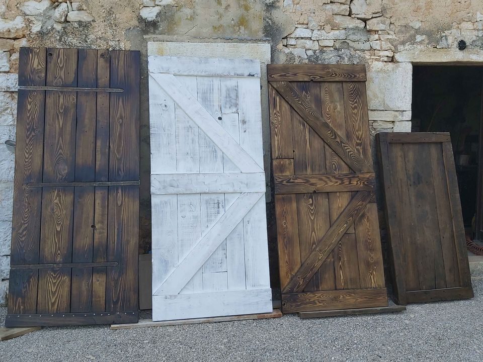 Quattro porte artigianali Portewestern di stili diversi, appoggiate a un muro in pietra